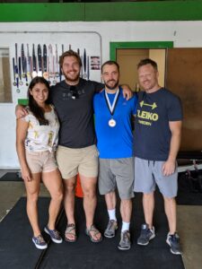 Four people standing in front of a wall of weightlifting medals